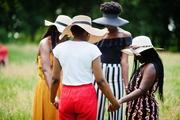 Négy gyönyörű afro-amerikai nőből álló csoport nyári kalapot visel kézen fogva és imádkozva a zöld fűben a parkban.. - Fotó, kép