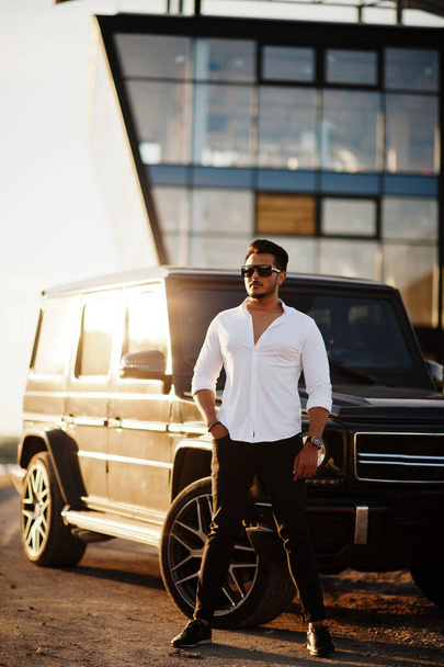 Solid asian man in white shirt and sunglasses posed near black mafia suv car.  - Фото, зображення