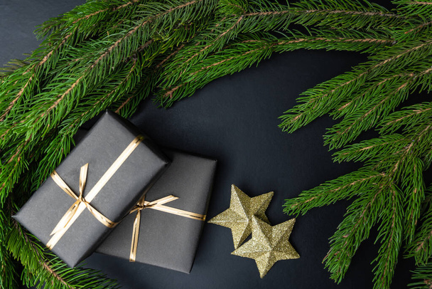 Siyah ambalajlı hediyeler iki altın yıldız ve köknar dalları siyah arka planda. Mutlu Noeller ve mutlu yıllar. Yakın plan.. - Fotoğraf, Görsel