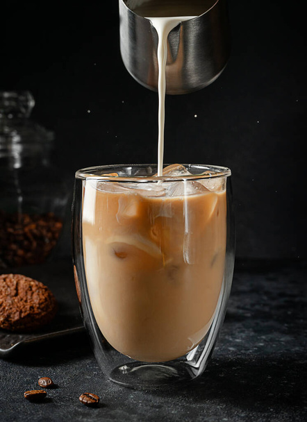 Pouring cream into the glass of iced coffee on black background. - Foto, imagen