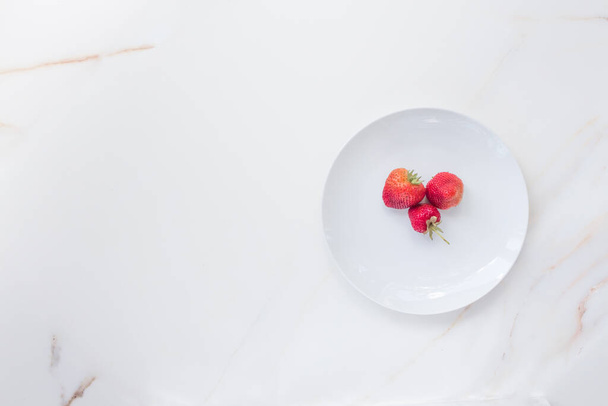  Three strawberries on a large white dish with copy space. The concept of spring and berries from your vegetable garden - Foto, Bild