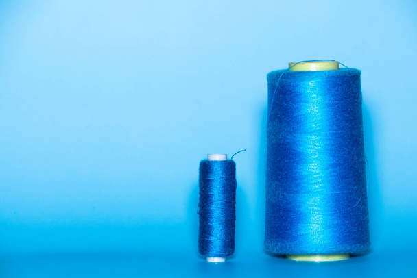 Background with a large and small blue spool of thread. They lie next to each other on a blue background. - Foto, immagini