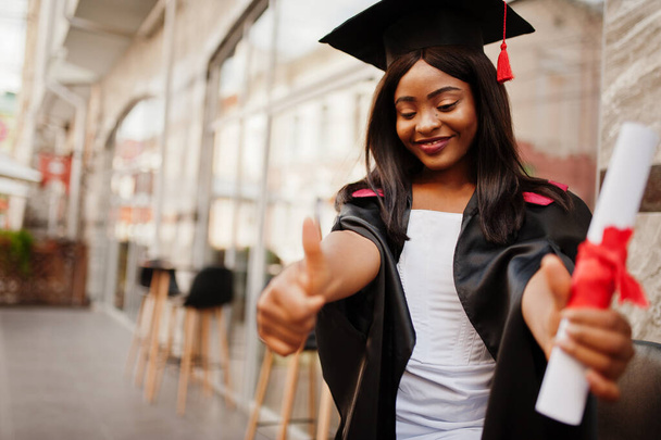 Joven mujer afroamericana estudiante con diploma posa al aire libre - Foto, imagen