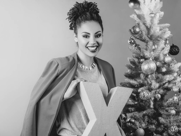 Vidám afro-amerikai nő rózsaszín X betűvel a kezében a karácsonyfa háttér. Karácsony, újév, boldogság, ünnep koncepció - Fotó, kép