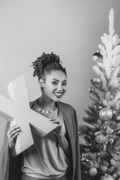 クリスマスツリーの背景にピンクの手紙Xを手にした陽気なアフロアメリカ人女性。クリスマス、新年、幸福、休日の概念 - 写真・画像