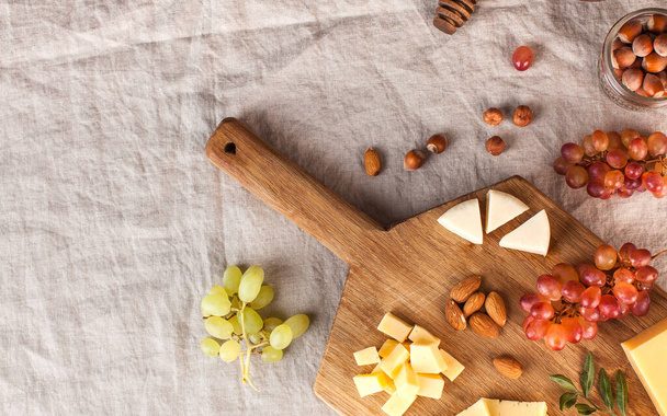 Cheese plate. Assorted cheeses on a wooden Board with grapes, honey, nuts on a linen tablecloth. High quality photo - Fotó, kép