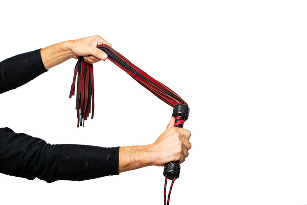 Leather whip in male hand. Man's hand is holding black and red bdsm lash on isolated on white. Accessories for adult sexual games. Toys for BDSM, flogging, sexual fetish and spanking devices with copy space. - Fotó, kép