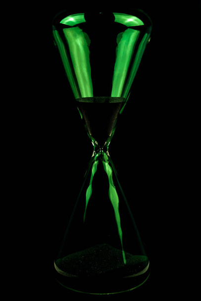 Concepto de tiempo de reloj de arena de vidrio verde sobre un fondo negro. Cuenta atrás concepto de tiempo simple - Foto, imagen