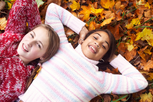 Dos chicas jóvenes tumbadas en hojas de otoño
 - Foto, Imagen