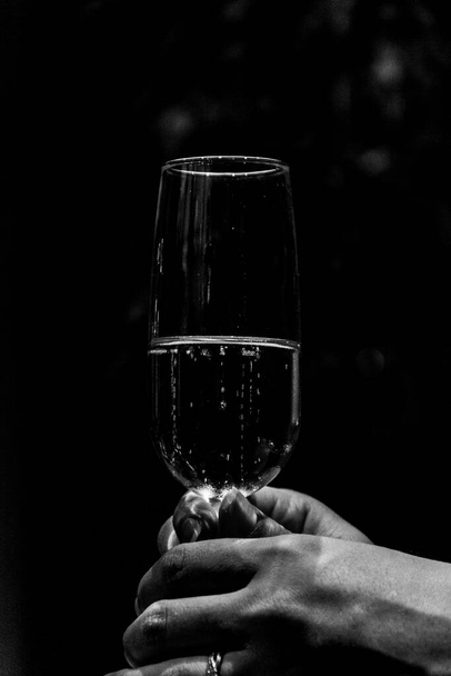 Черно-белый портрет бокала игристого шампанского, который держит женщина в руках с кольцом вокруг пальца на вечеринке. - Фото, изображение