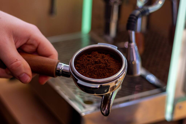 Portret baristy trzymającej portafilter kawy ze świeżymi fusami kawy w nim gotowy do zaparzenia kawy w ekspresie do kawy. - Zdjęcie, obraz