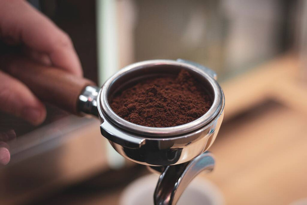Un retrato de cerca de un portafilter lleno de café molido de granos de café recién molidos. - Foto, imagen