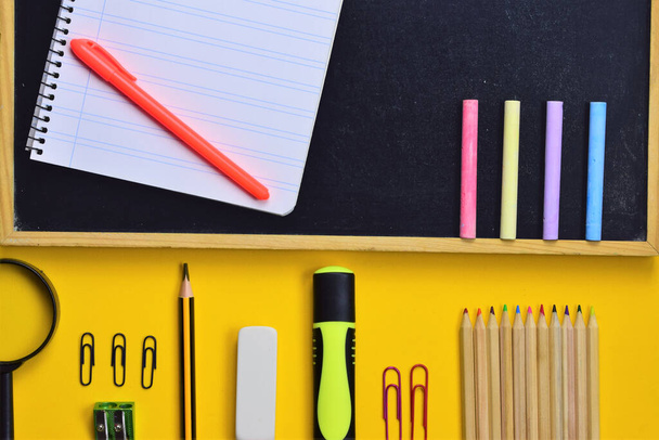 Varied school supplies from small blackboard with chalks and daily supplies at school, on yellow background - 写真・画像