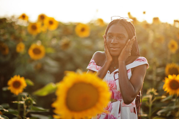 Pretty young black woman wear summer dress pose in a sunflower field. - Foto, Imagem