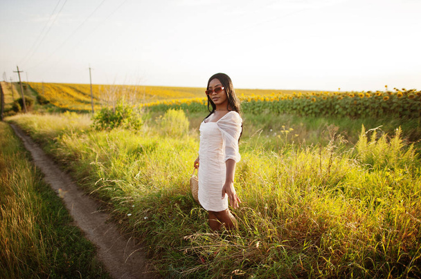 Pretty young black woman wear summer dress pose in a sunflower field. - Foto, afbeelding