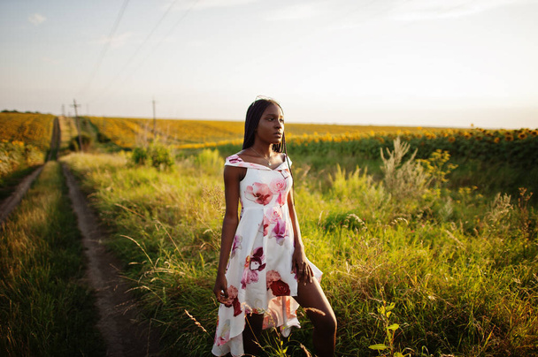 Pretty young black woman wear summer dress pose in a sunflower field. - Photo, Image