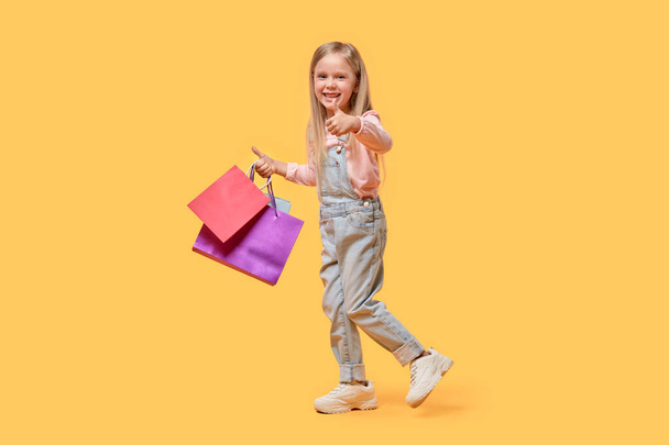 Beautiful blonde girl holding gifts in bags and showing a thumbs up gesture. - Foto, Imagem