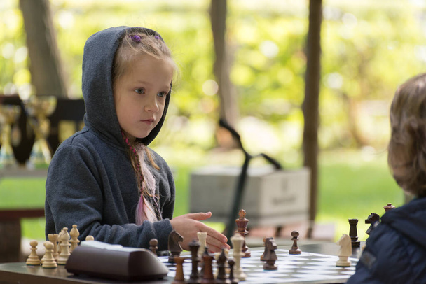 Beautiful Smart Girl, seven years old is taking part a kids chess tournament outdoor in the park. - 写真・画像