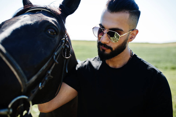Arab tall beard man wear in black and sunglasses with arabian horse. - Fotó, kép