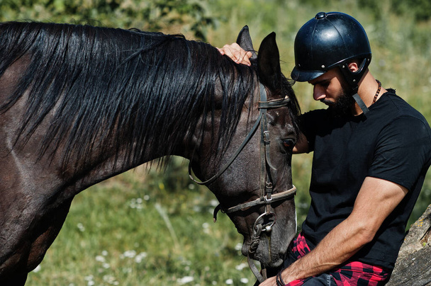 Arab tall beard man wear in black helmet with arabian horse. - Zdjęcie, obraz