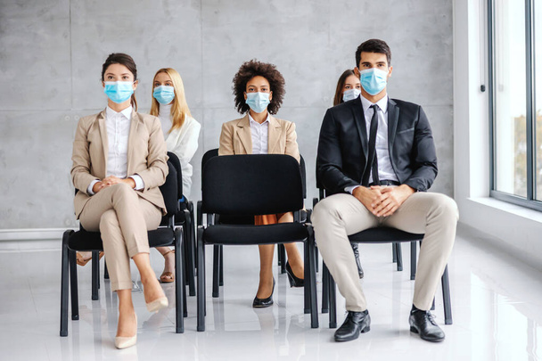 Multicultural group of business people with face masks sitting on seminar and listening during corona outbreak. - Foto, Bild