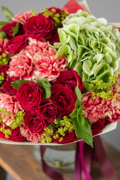Rode en groene bloemen. Herfst boeket van gemengde bloemen in glazen vaas op houten tafel. Het werk van de bloemist in een bloemenwinkel. Verse snijbloem. - Foto, afbeelding