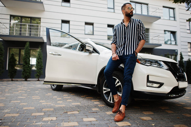 Successful arab man wear in striped shirt and sunglasses pose near his white suv car. Stylish arabian men in transport. - Foto, Bild