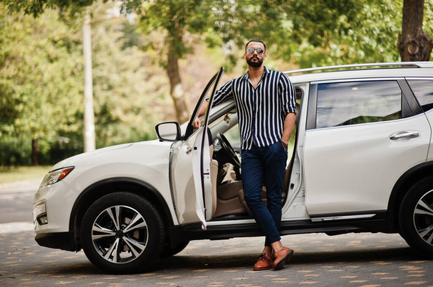 Successful arab man wear in striped shirt and sunglasses pose near his white suv car. Stylish arabian men in transport. - Foto, imagen