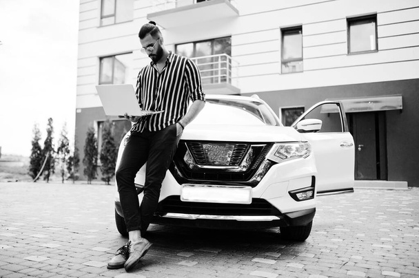 Successful arab man wear in striped shirt and sunglasses pose near his white suv car with laptop in hand. - Fotografie, Obrázek