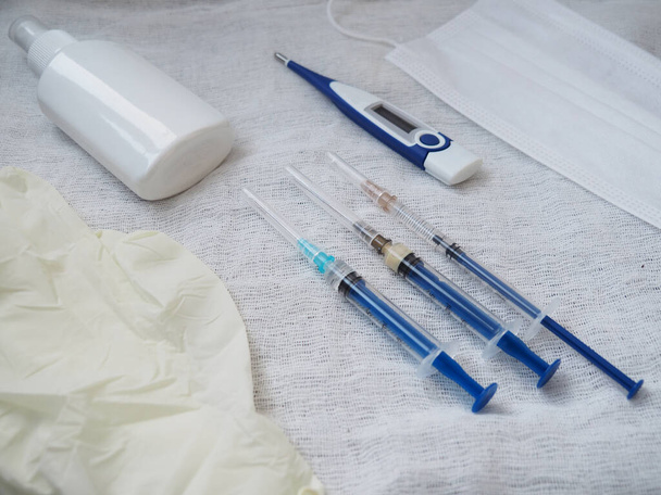 Медичний шприц, електронний термометр, медична маска, одноразові рукавички та антисептик на білому тлі
 - Фото, зображення