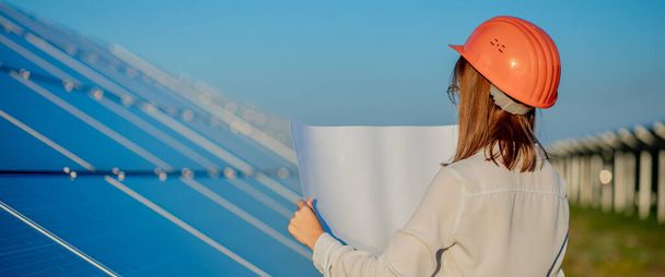 Handsome Architect Woman Examining a Draft Map or Blueprint Project Plan, Worker Activity Looking Out in Photovoltaic Cell Farm or Solar Panels Field. - Foto, afbeelding