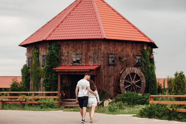 Coppia innamorata cammina vicino a un grande mulino di legno il giorno d'estate. uomo e donna si divertono all'aperto - Foto, immagini