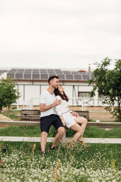 Coppia amorevole è seduto nel parco estivo sulla recinzione bianca. uomo e donna si stanno abbracciando all'aperto in una giornata calda. - Foto, immagini
