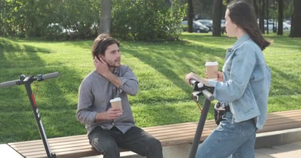 Φίλοι μιλάμε με φλιτζάνι καφέ και e σκούτερ στο πάρκο - Πλάνα, βίντεο