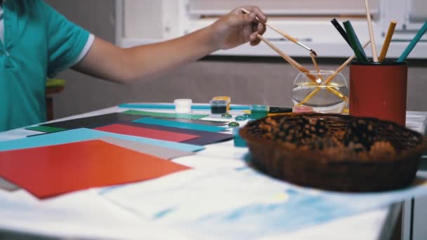 子供の手は、テーブルの上にブラシ、水彩画、はさみをレイアウトします。ボーイアーティスト - 映像、動画