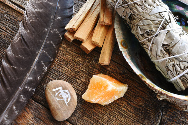 Una imagen de vista superior del palo de mancha de salvia blanca con cristales curativos, pluma sagrada y símbolo de reiki. - Foto, imagen