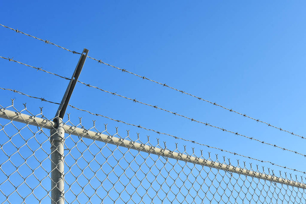 Abstraktní obraz vysokého průmyslového plotu s ostnatým drátem proti jasně modré obloze.  - Fotografie, Obrázek