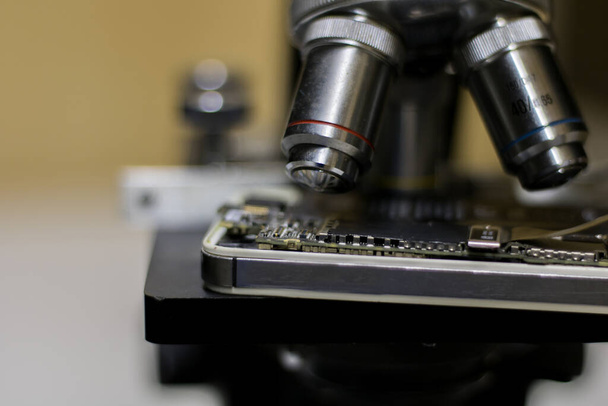 κοντινή εμπρόσθια όψη μικροσκοπίου, κατά την ανάλυση των ηλεκτρικών κυκλωμάτων κινητού τηλεφώνου. - Φωτογραφία, εικόνα