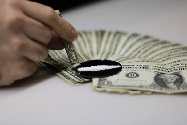 Vista frontal y de cerca de un fan de los billetes de dólar derivados del comercio de cocaína, mientras que una tira de cocaína se inhala en un espejo. - Foto, Imagen