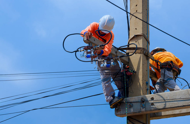 2 eletricistas com equipamentos de segurança estão trabalhando para instalar o sistema elétrico no polo de energia contra o fundo do céu azul - Foto, Imagem
