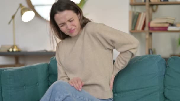 Νεαρή γυναίκα με πόνο στην πλάτη κάθεται στον καναπέ  - Πλάνα, βίντεο