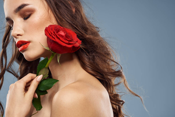 Portrait of a woman with a red rose in her hands on a gray background naked shoulders evening makeup - Photo, Image