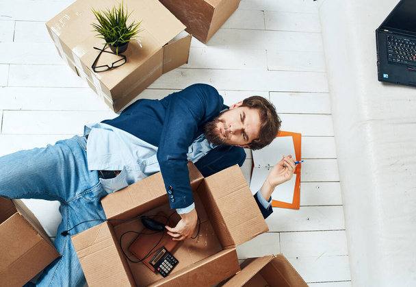 Un uomo con scatole si trova sul pavimento di una stanza di trasloco ufficio disimballaggio - Foto, immagini