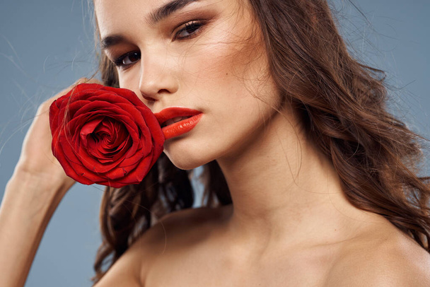 Portret kobiety z czerwoną różą w dłoniach na szarym tle nagie ramiona makijaż wieczorowy - Zdjęcie, obraz