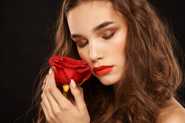 mujer con una rosa roja sobre un fondo oscuro pelo largo maquillaje labios rojos - Foto, imagen