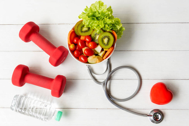 Health Care.  Fresh vegetable salad with medical stethoscope and equipment dumbbell for diet and weight loss for healthy care and protect virus,  white wooden background.  Healthy Life Concept - 写真・画像