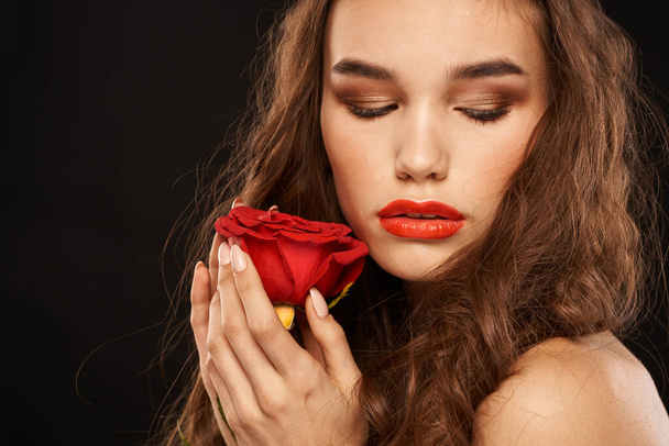 Frau mit roter Rose auf dunklem Hintergrund lange Haare Make-up rote Lippen - Foto, Bild