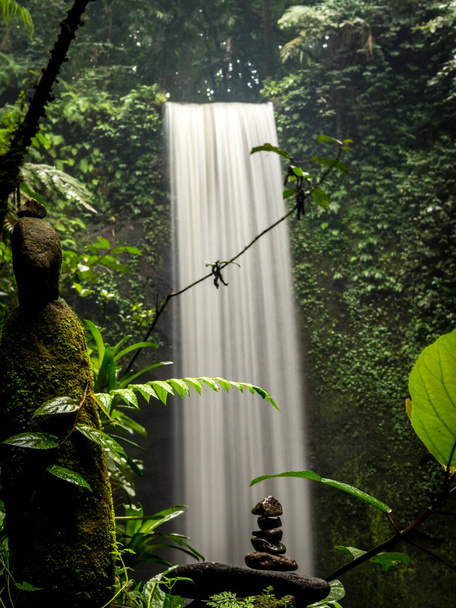 Vesiputous lähellä. Rauhallinen luonto. Tasapaino kiviä. Kaunis maisema. Trooppinen metsä. Liikevettä. Hidas suljinnopeus. Pystysuora asettelu. Tibumanan vesiputous Balilla, Indonesiassa - Valokuva, kuva