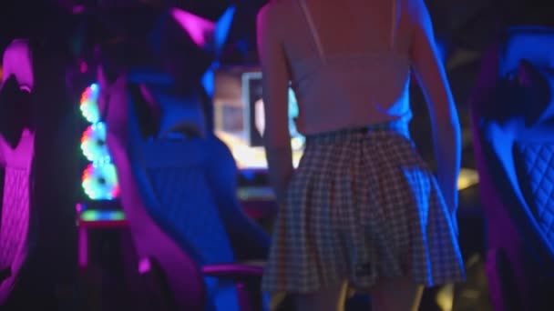 Młoda kobieta w spódnicy idzie do komputera w klubie gier i siada na krześle - Materiał filmowy, wideo