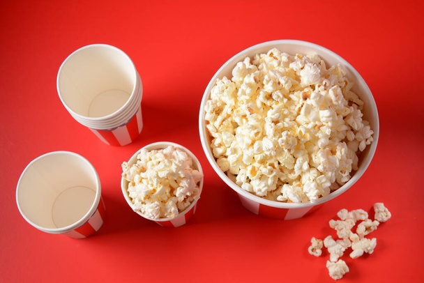 Buckets with delicious popcorn on red background. Spilled popcorn  - Photo, Image